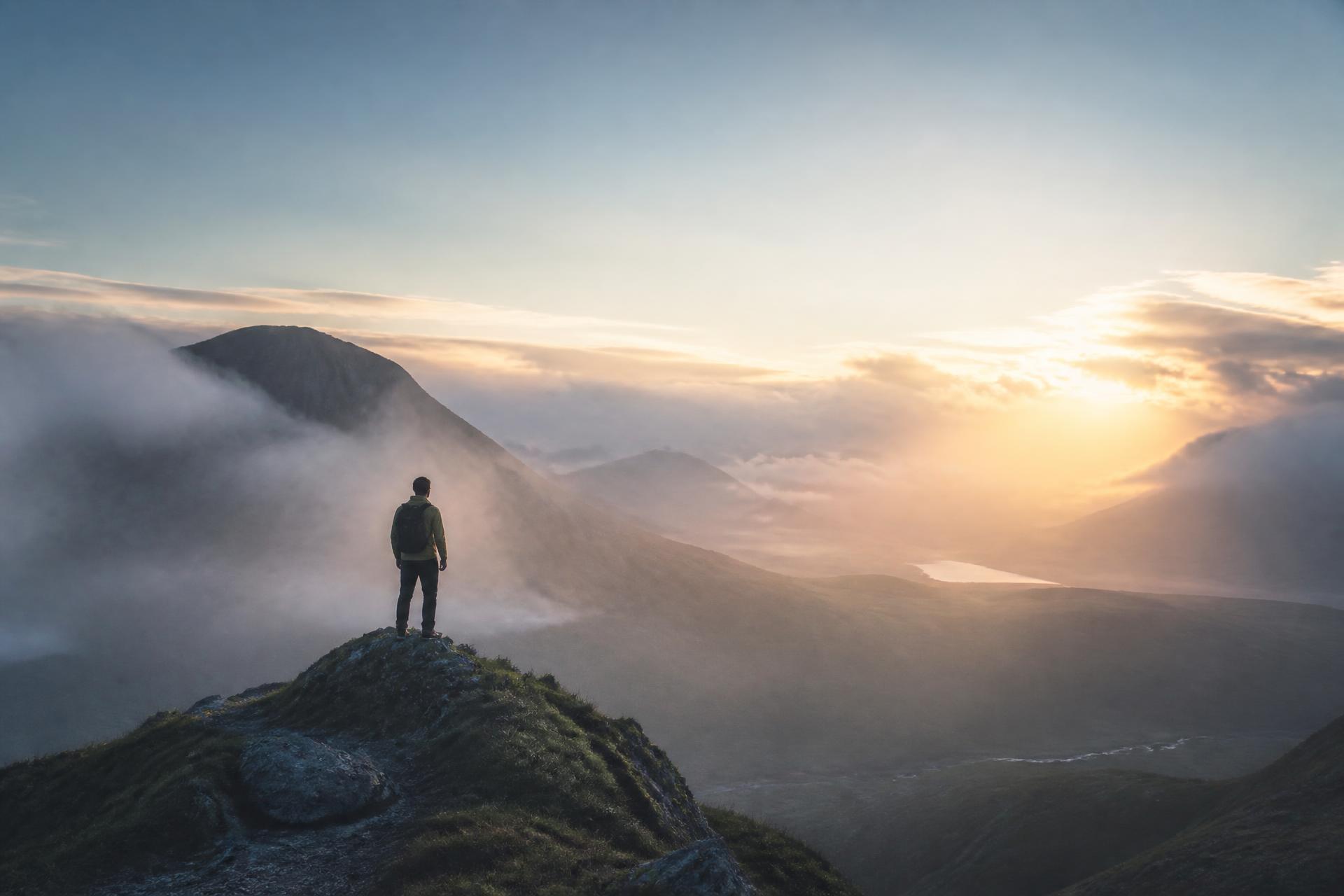 A lone hiker on a misty mountain peak at dawn